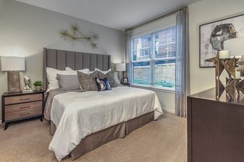 A bedroom with a large bed and a nightstand with a plant on it at Crabtree Lakeside Apartments, Raleigh, North Carolina